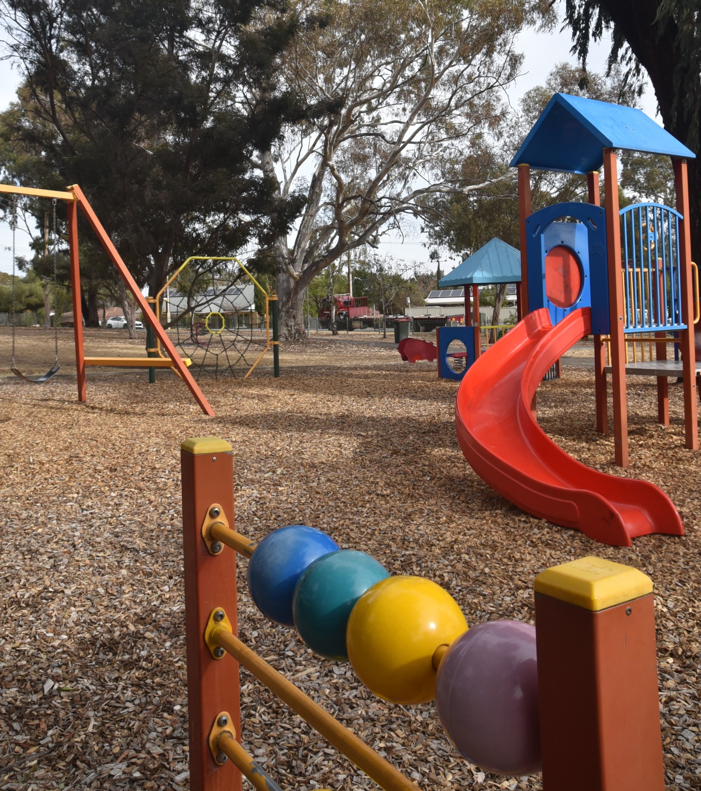 Red slide coming off small fort with swing and spider web climbing frame in background. Counting beads on a frame in the foreground