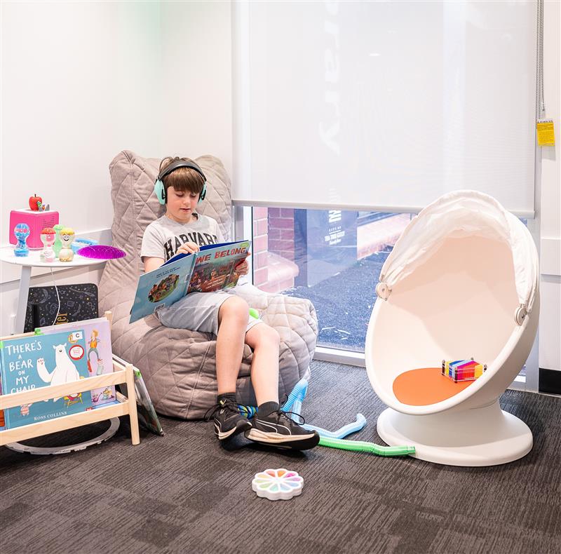Boy sitting in a bean bag chair. He is wearing headphones and reading a book