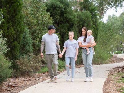 Family walking along a path. A man is holding a young girl's. A woman is holding a toddler